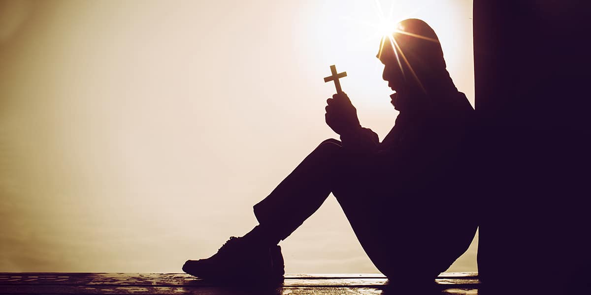 man sitting in meditation while holding a cross with both hands.