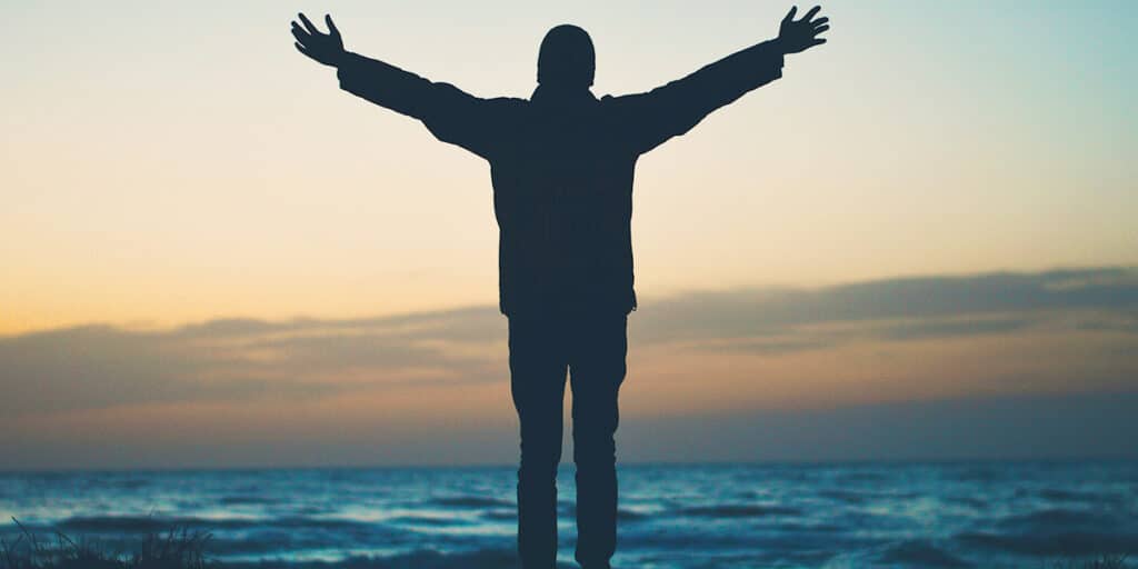 man standing on a beach with his hands raised