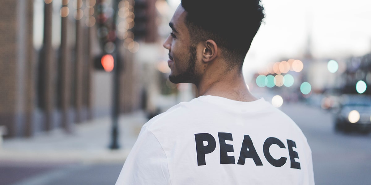 man wearing a white shirt with the word peace printed on the back.