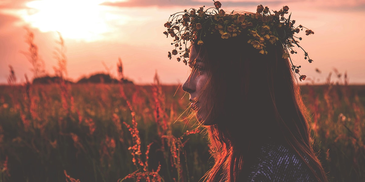 woman wearing a flower crown standing in a field during sunset.