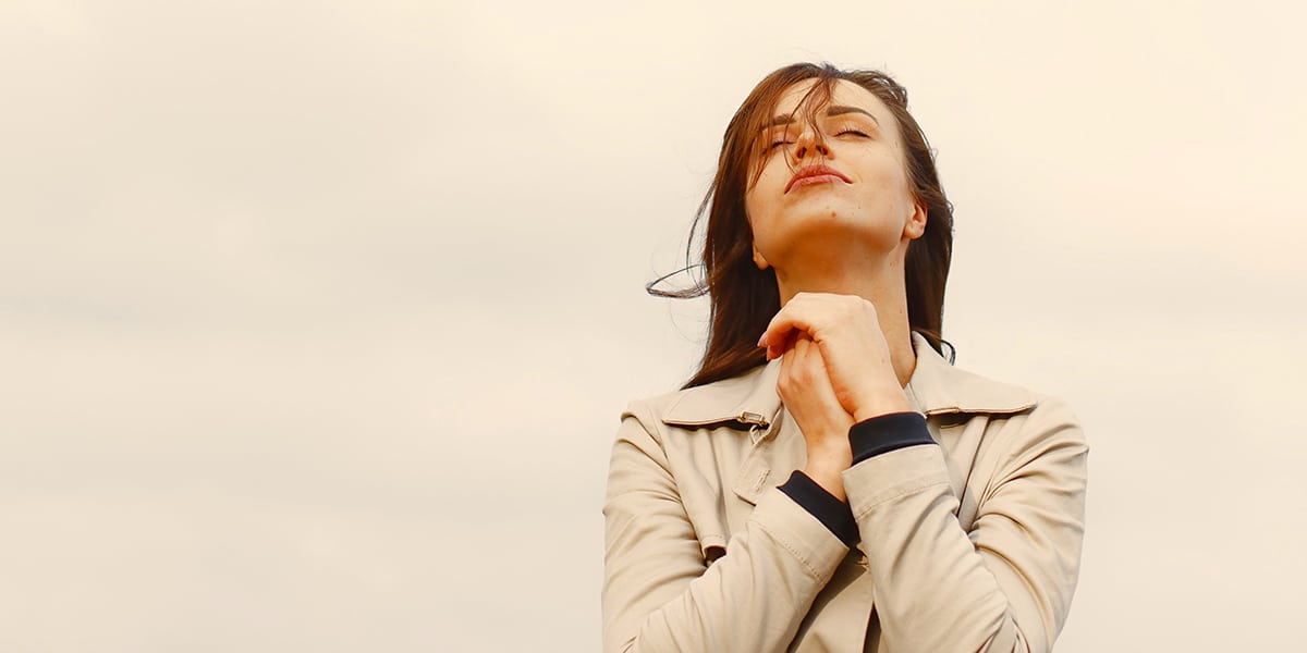 woman in a pasture of gratitude, eyes closed and hands folded.