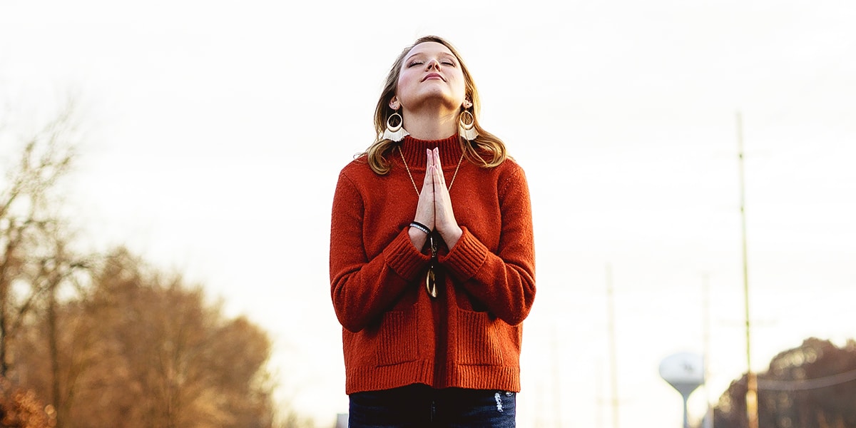 woman hands folded and eyes closed in prayer with a hopeful expression on her face.