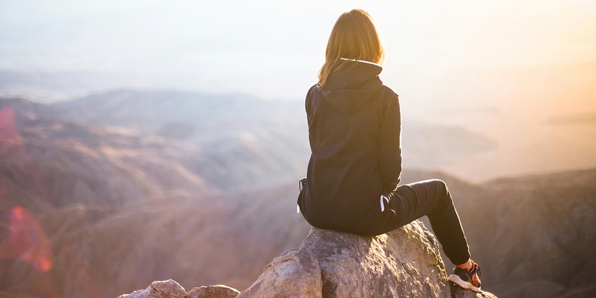 woman sitting on a rock and looking in the valleys below, during a sunset