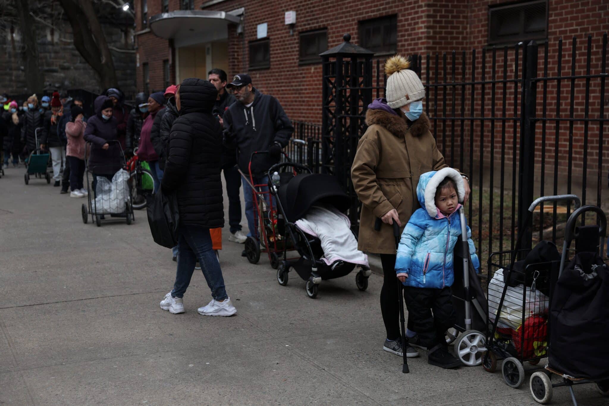 People wait in line to receive food donations from Catholic Charities services along 105th street in the East Harlem area of New York City, Feb. 22, 2023.