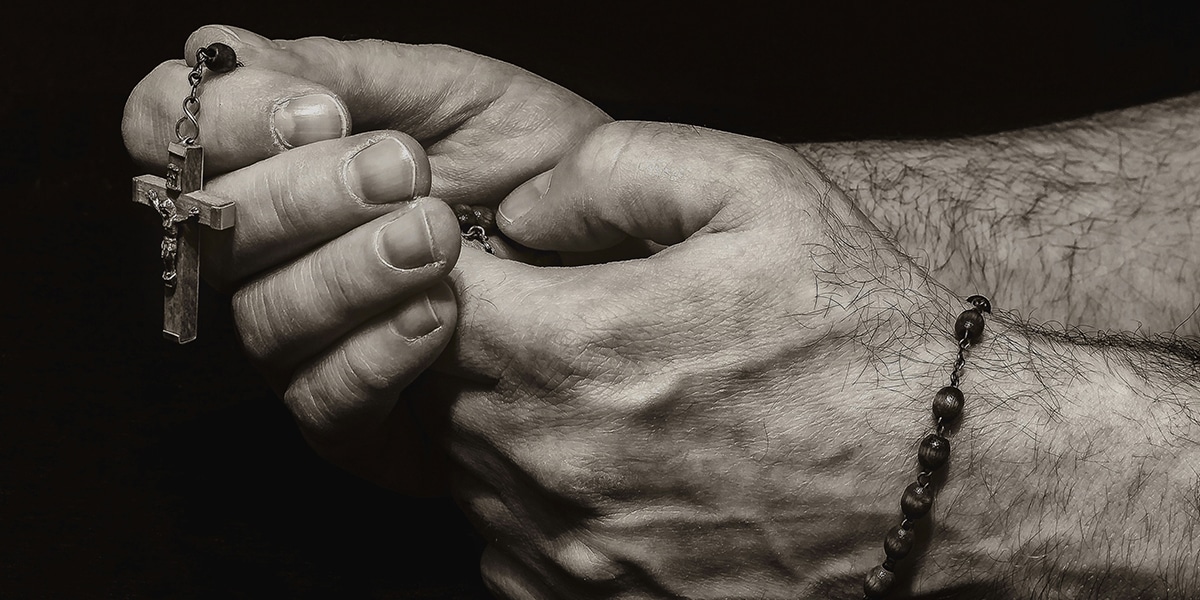 hands folded in prayer while holding a rosary