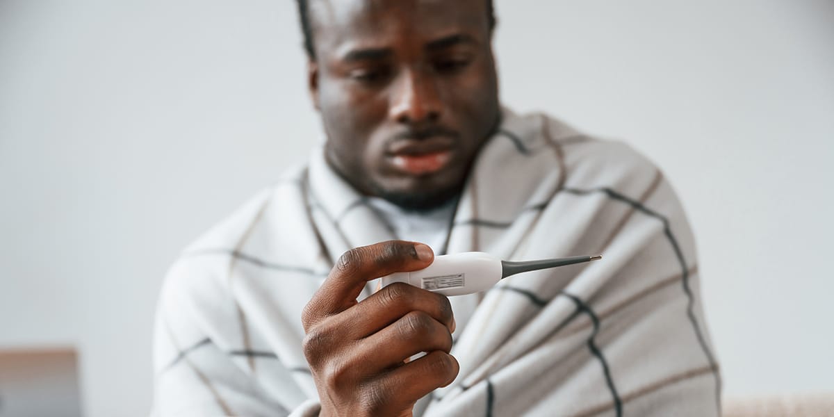 man checking his fever with a thermometer.