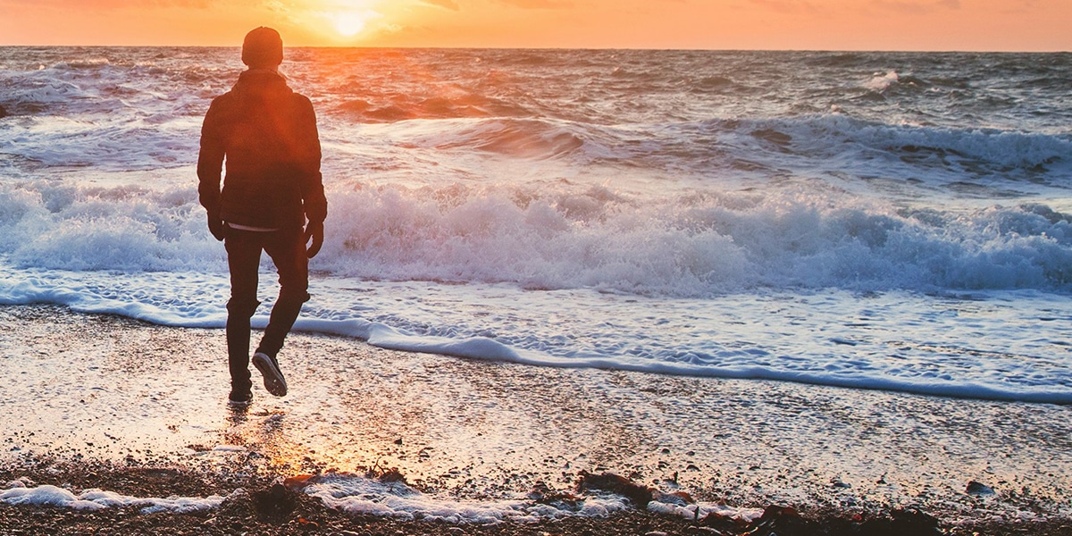 man walking on beach while waves crashing