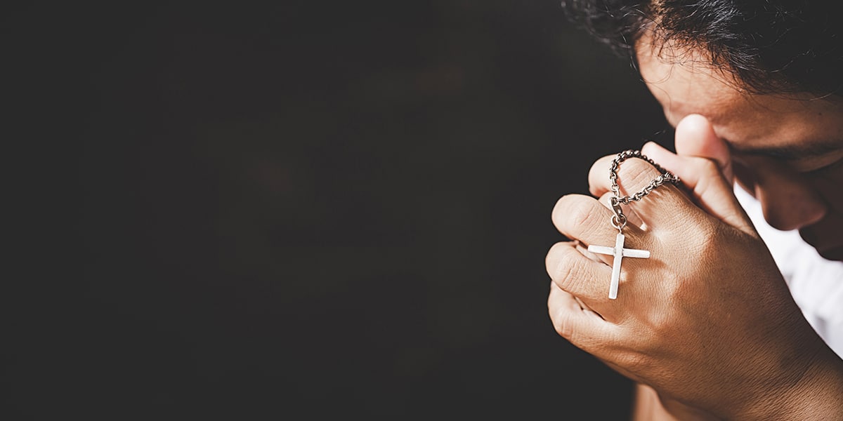 person praying with folded hands while holding a rosary