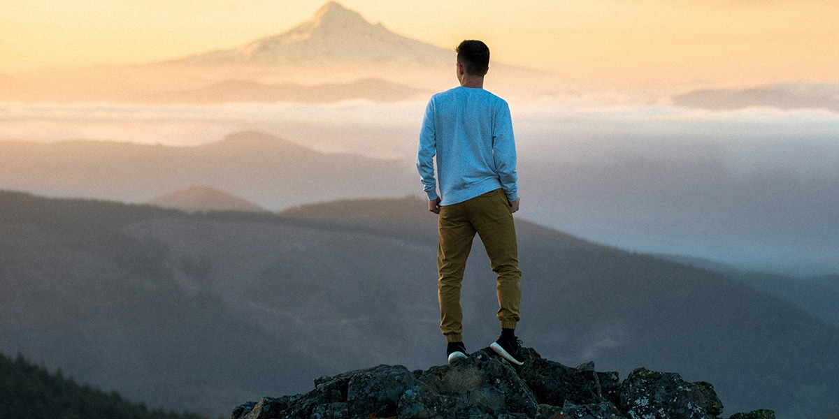 Young man standing on top of a mountain, above the clouds