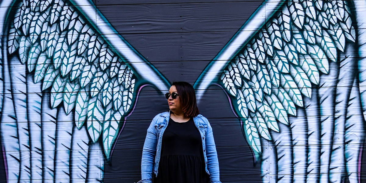 woman standing in front of painted angel wings on a wall