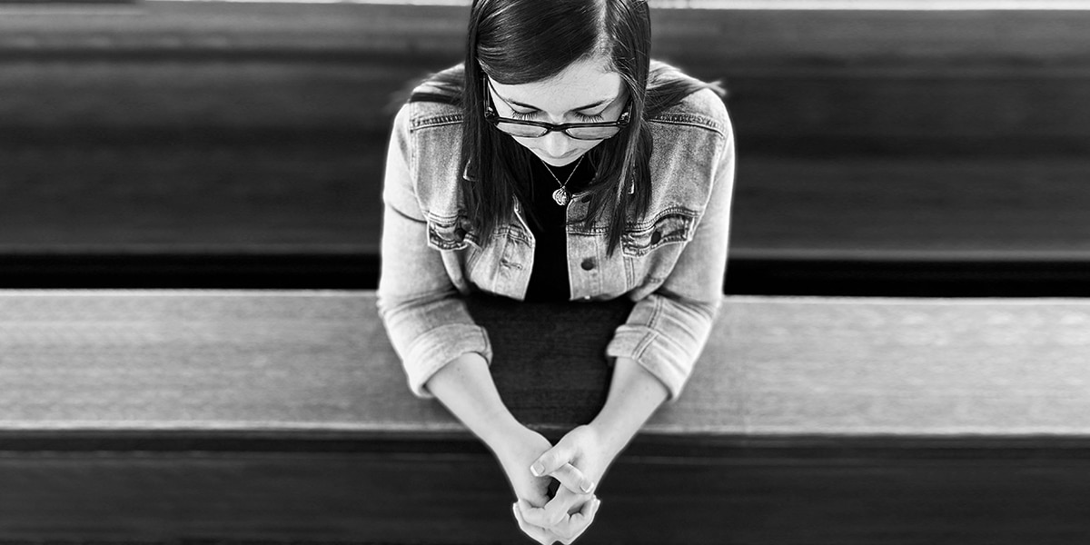 woman sitting in a church pew with folded hands