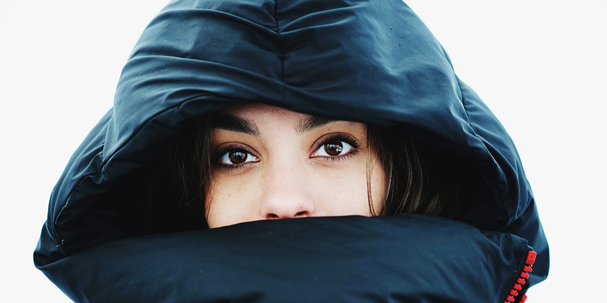 woman wearing a winter jacket with a hoody, covering most of her face, showing her wide open eyes.