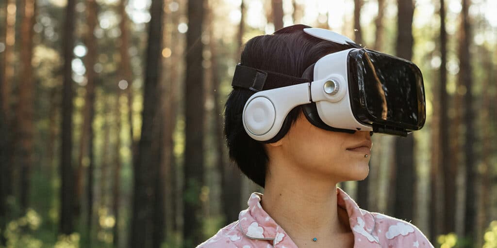 woman standing in front of a forest, wearing VRglasses and looking into the digital future.