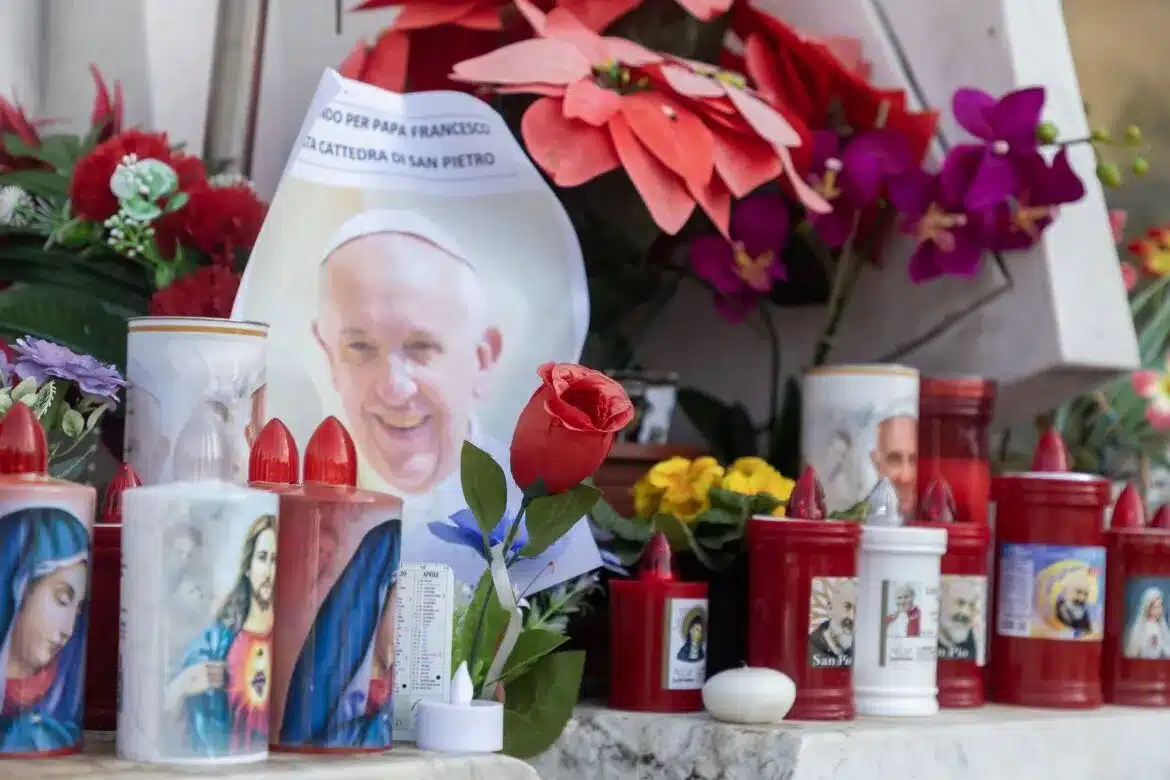 Votive candles and flowers are seen at the base of a statue of St. John Paul II outside Rome's Gemelli hospital Feb. 23, 2025, where Pope Francis is being treated for double pneumonia. (CNS photo/Pablo Esparza)