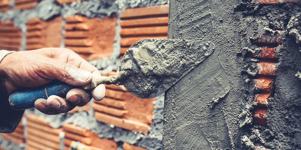 hand using a trowel to put cement on a brick wall