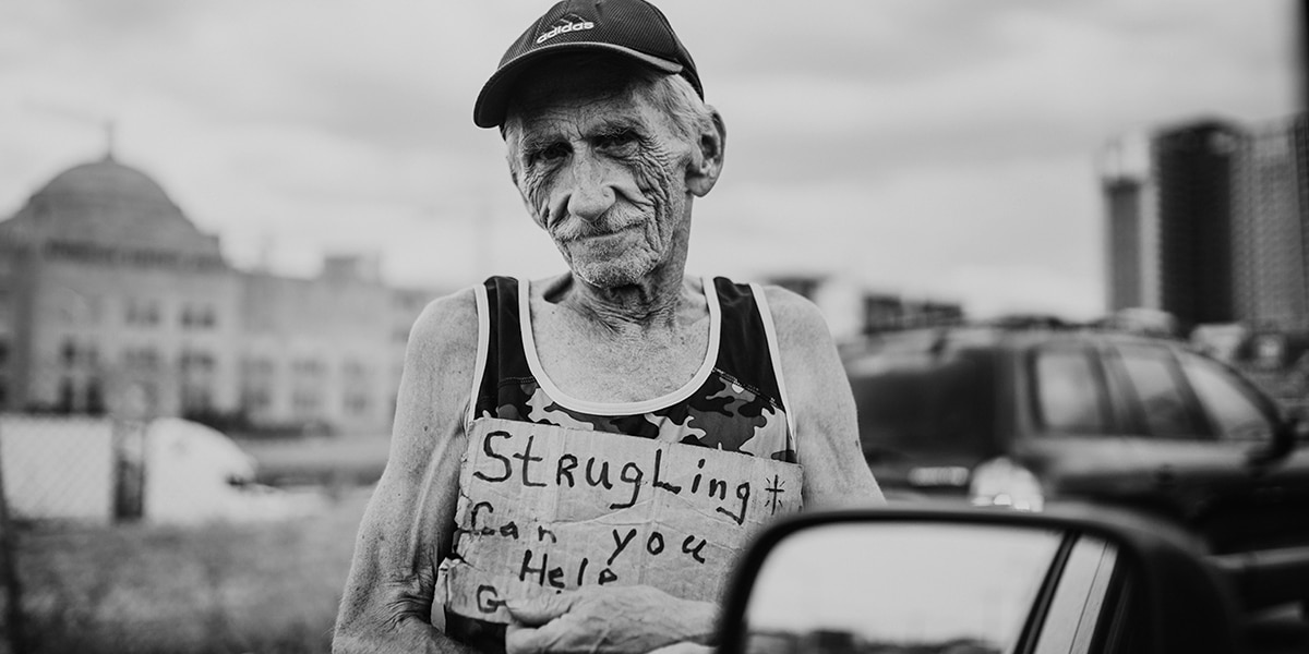 homeless man holding a sign "Struggling, can you help?"