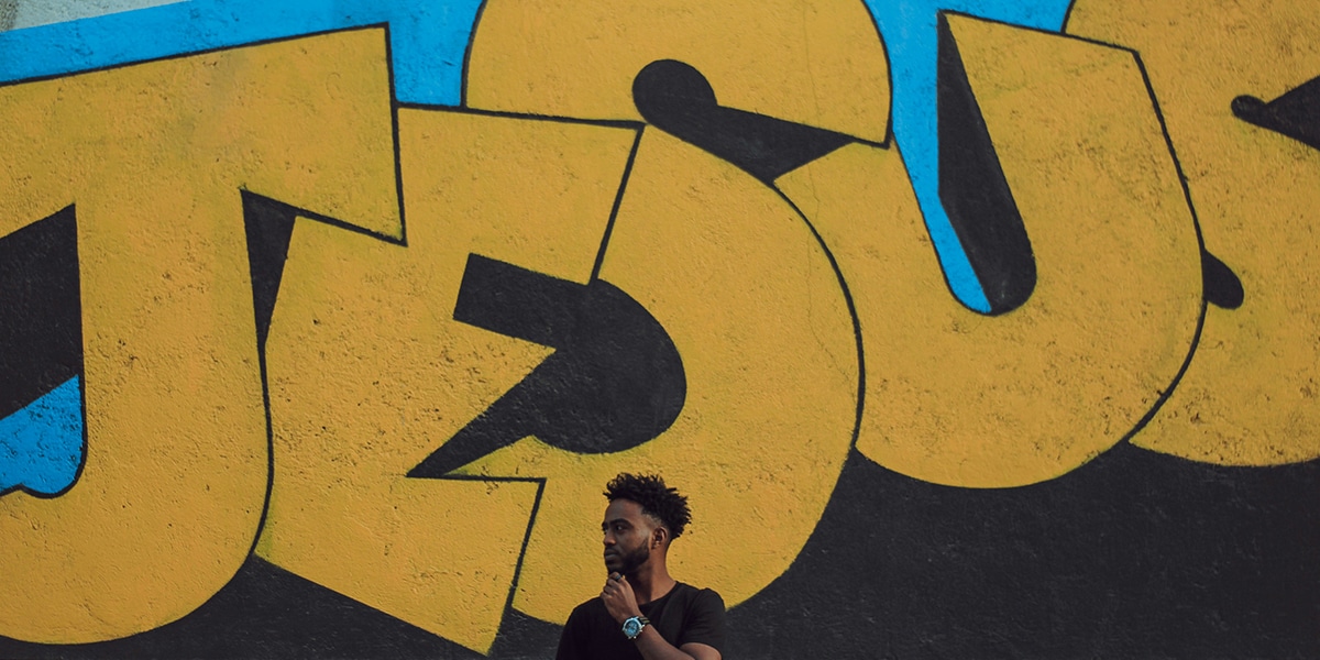 Man standing in front of graffiti with the word Jesus