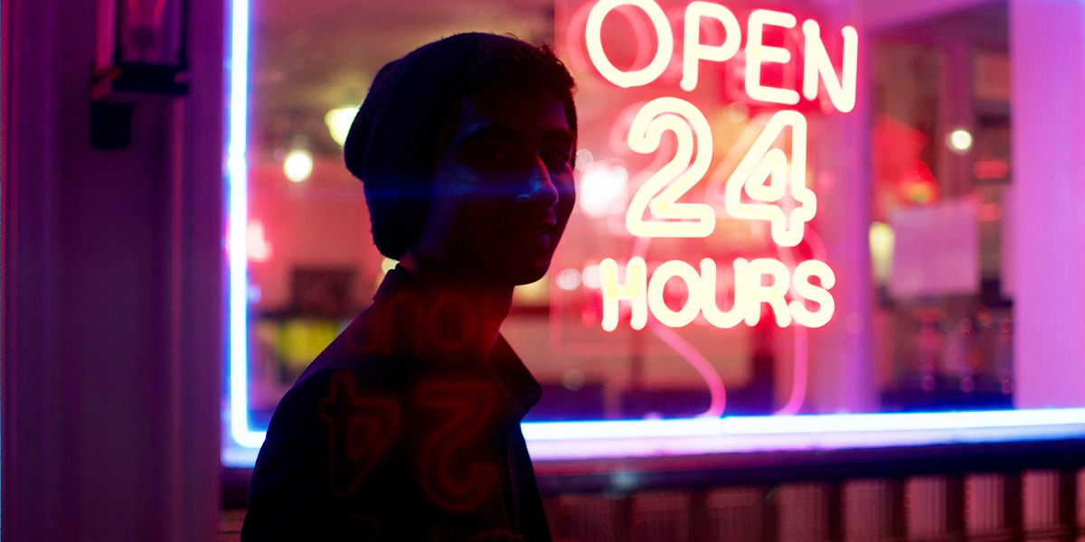 person in front of a open twenty four hours neon sign.