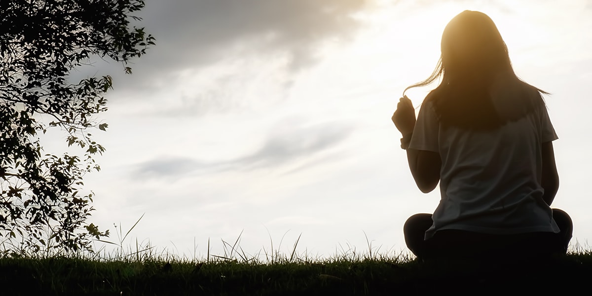 woman with a hallow around her head is sitting in a field