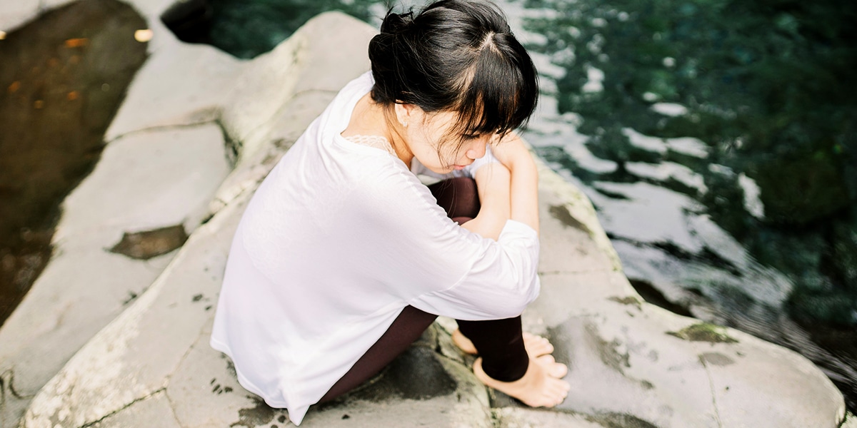 woman sitting on a rock while praying and reflecting