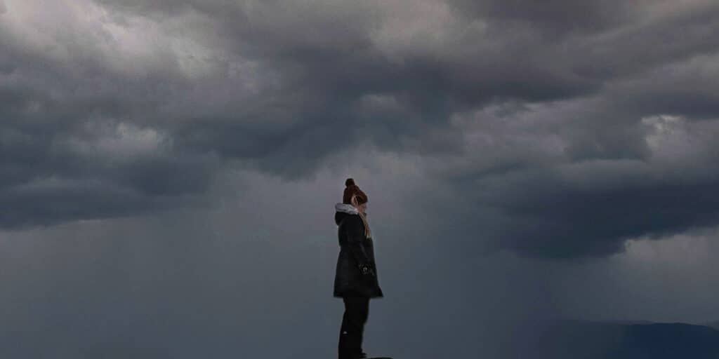 woman standing in a storm, surrounded by dark clouds and rain