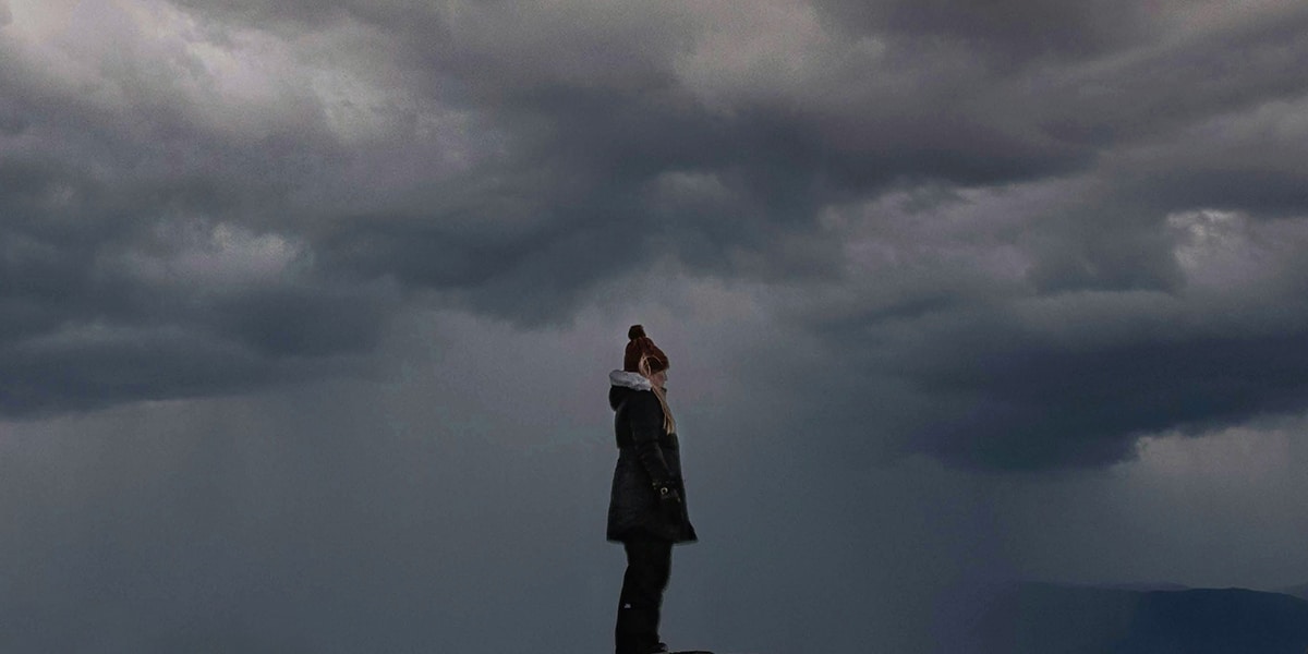 woman standing in a storm, surrounded by dark clouds and rain