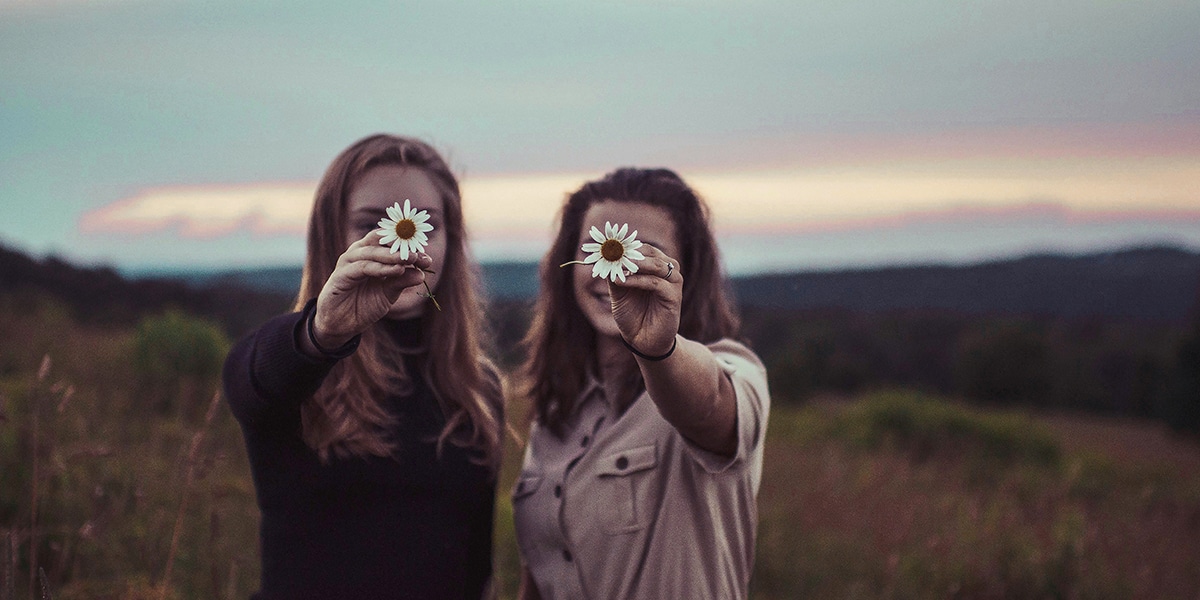 two women standing in a field and holding each a flower