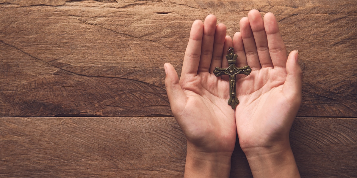 Open hands holding a metal cross