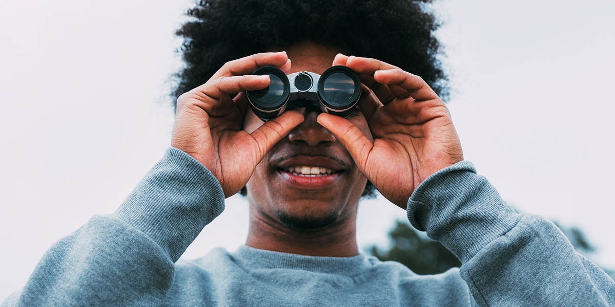 young man searching, focusing in with binoculars