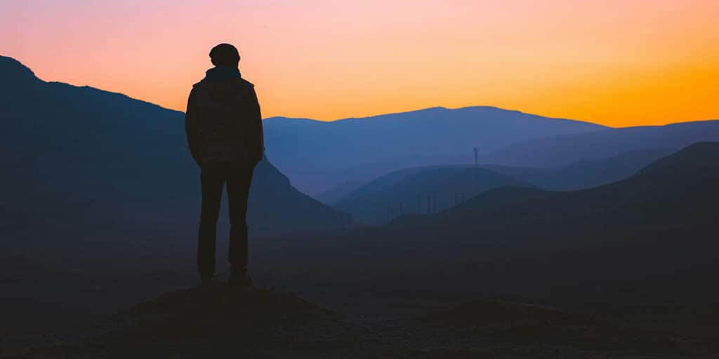 man standing silently on a mountain and watching a sunset.