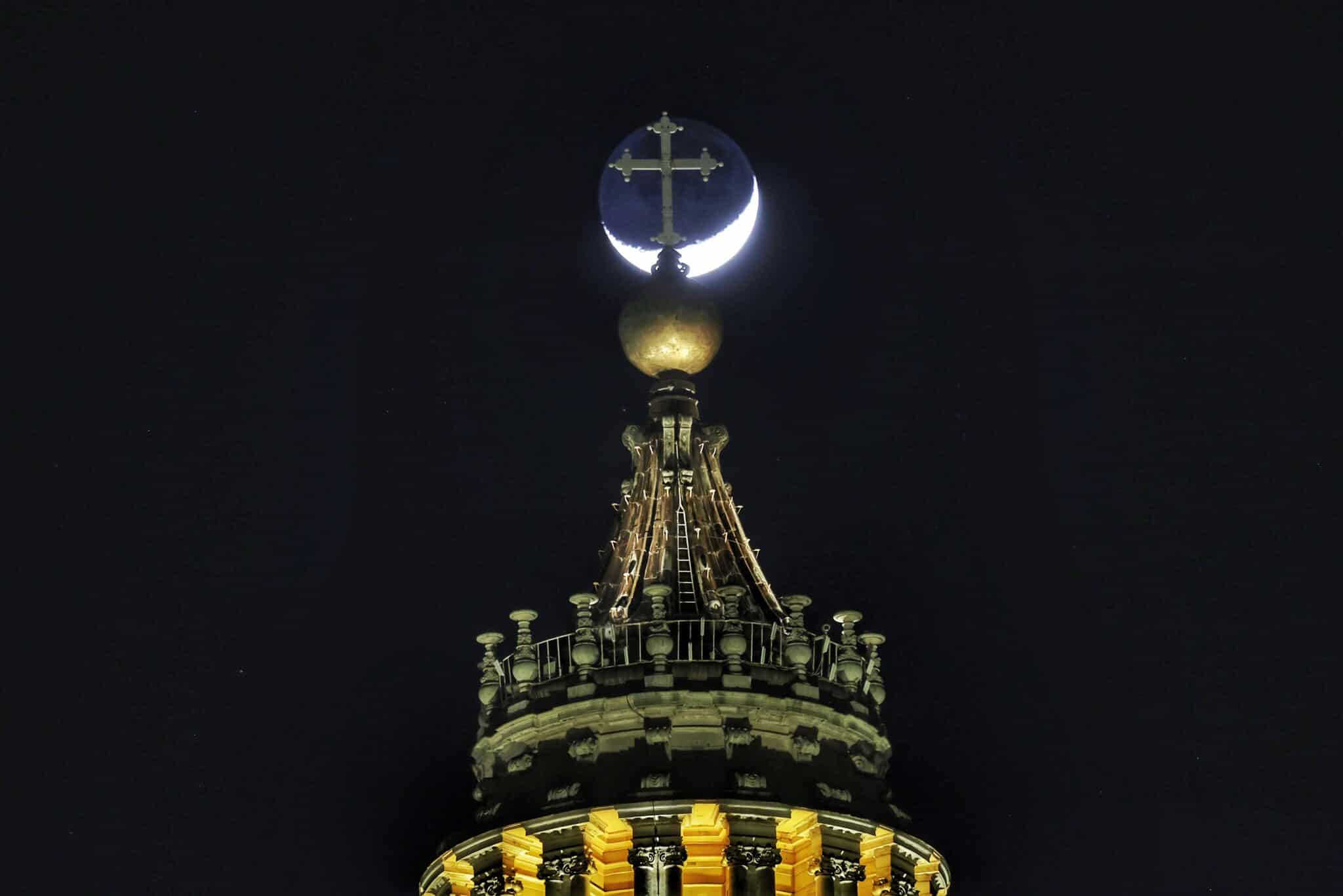 The moon is seen behind the cross on top of the dome of St. Peter's Basilica at the Vatican as people gather to pray the rosary for Pope Francis in St. Peter's Square March 3, 2025. (CNS photo/Pablo Esparza)