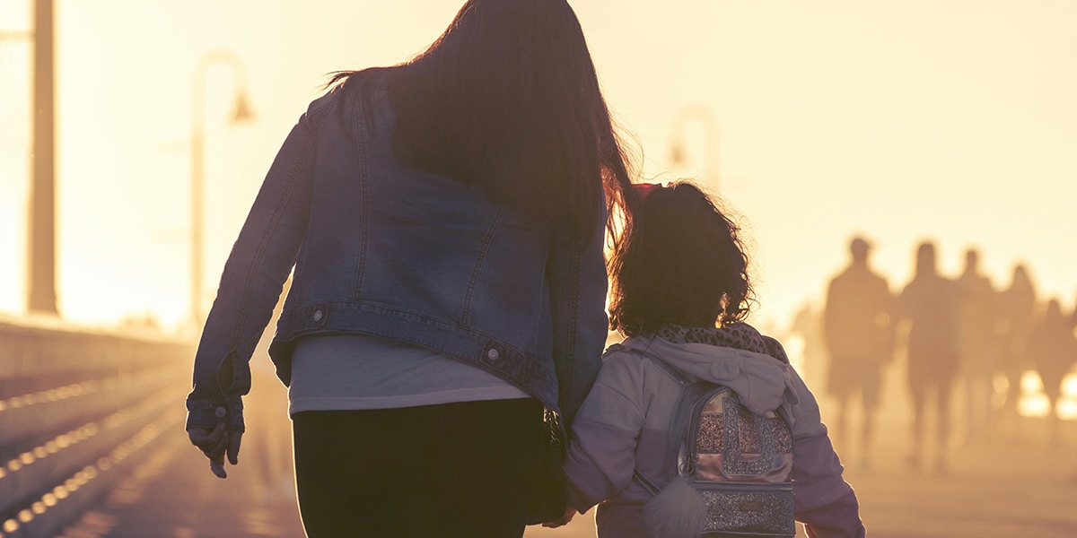 a parent holding hands with a child surrounded by sunlight.